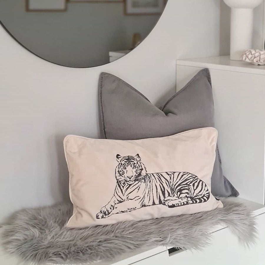 Beige prydnadekudde med tiger motiv liggandes på en hallbänk
