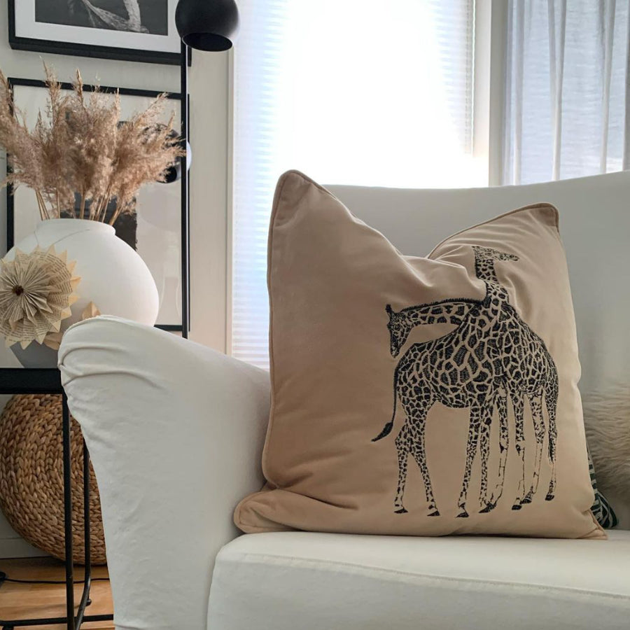 prydnadkudde med broderad giraff på framsidan, kudden ligger i en vit soffa.