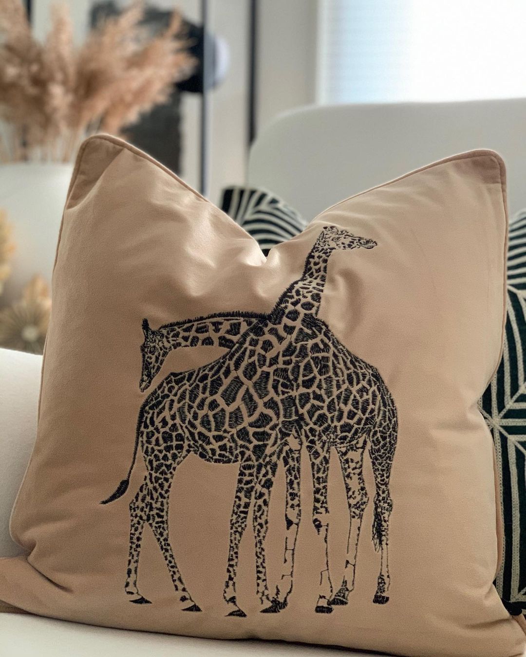 beige prydnadskudde med motivet av en broderad giraff på framsidan.