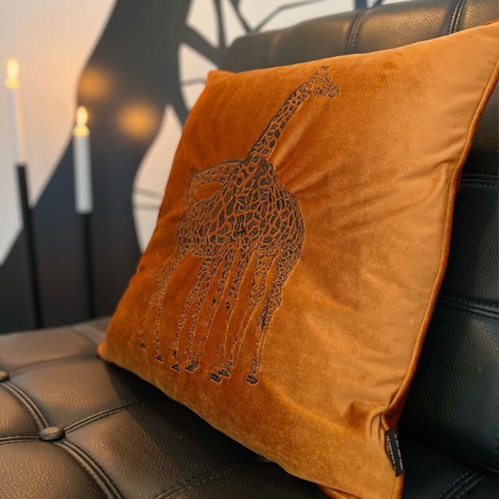 roströd prydnadskudde med motivet av en giraff, i en svart soffa